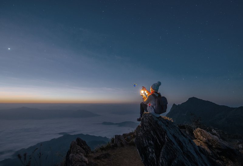 person sitting holding a light outdoors mountaintop starry night 