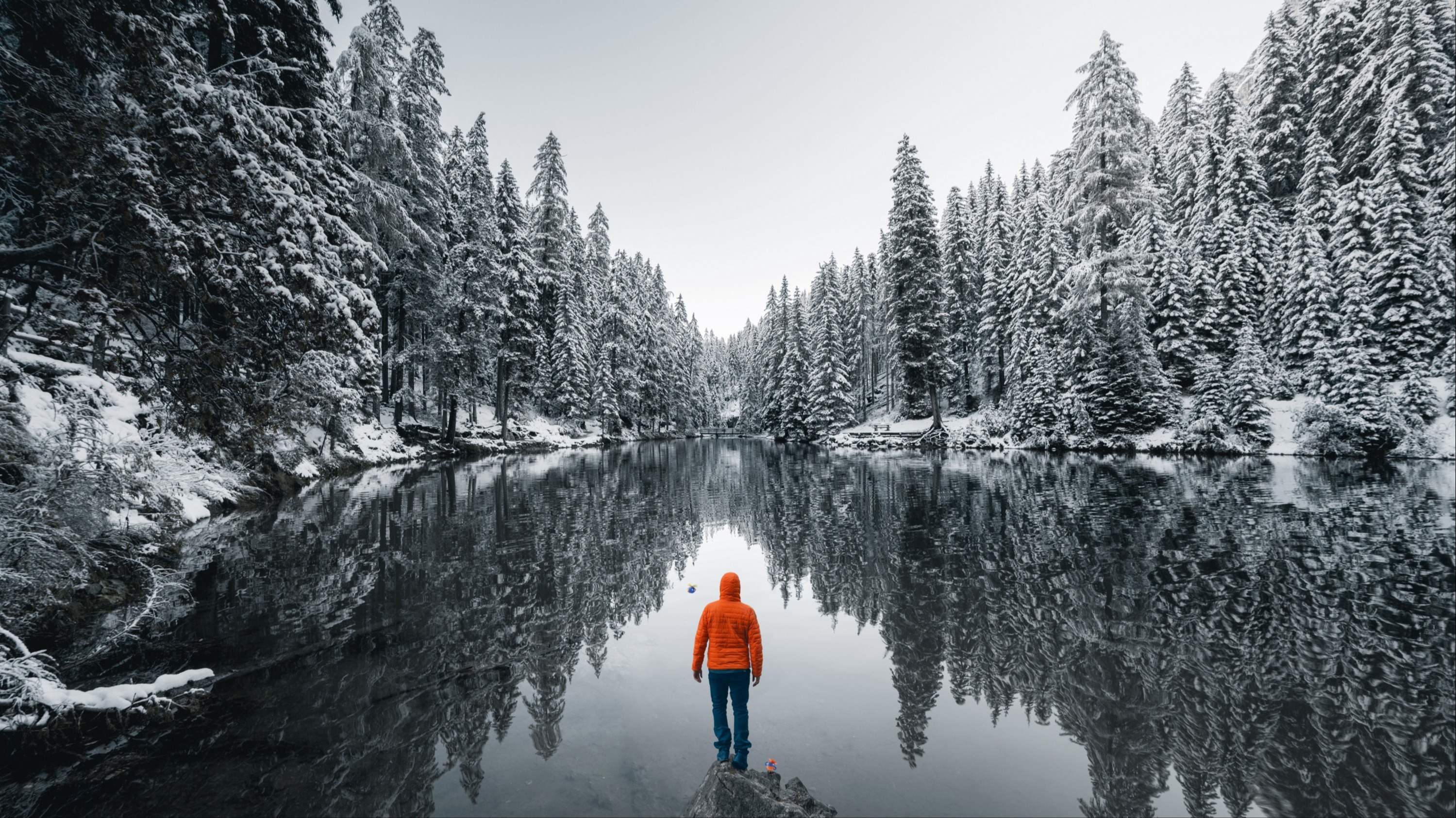 A person in an orange jacket looking at a lake into a valley.