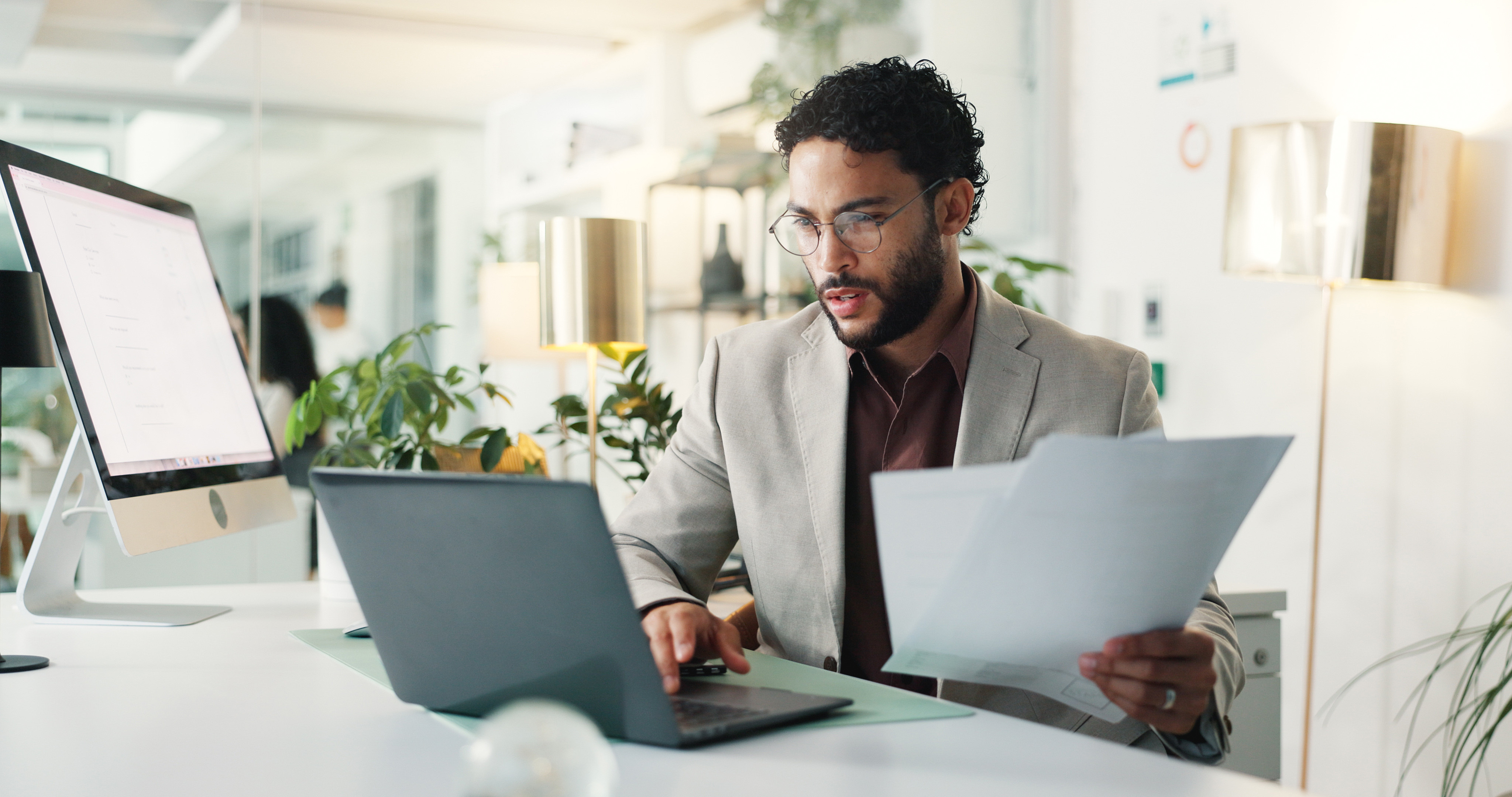 office worker sitting at a desk using a laptop and reviewing documents