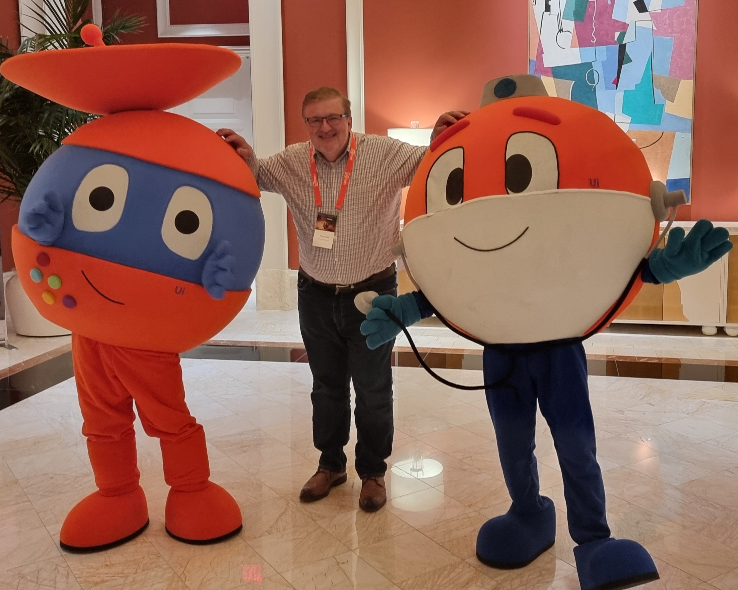 Tony Nudd smiling and standing between two large, colorful UiPath bot mascots