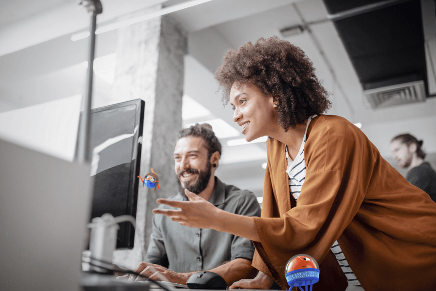 two people at a desk looking at a monitor
