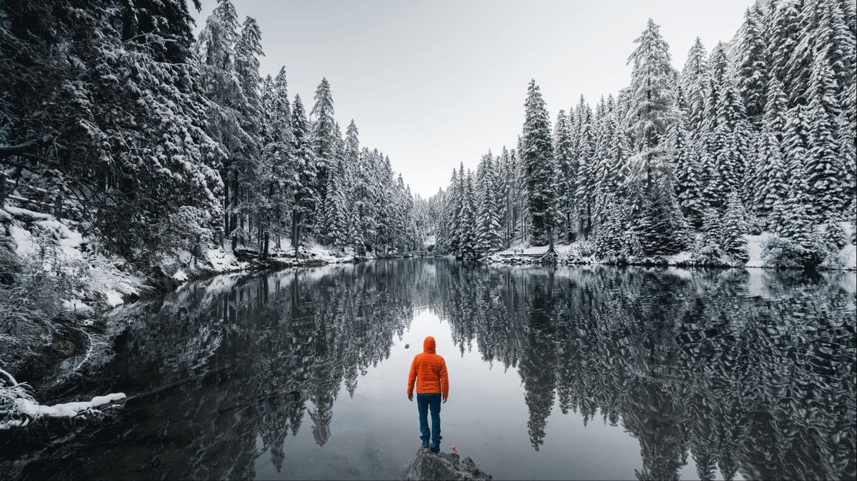A person in an orange jacket looking at a lake into a valley.