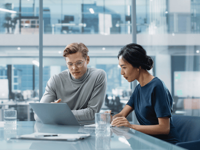 two people sitting at a table looking at a laptop