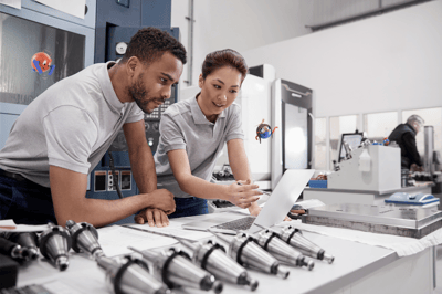 two people standing at a desk looking at a laptop manufacturing