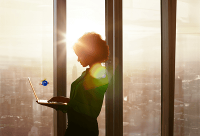 woman standing holding a laptop with city skyline in the background