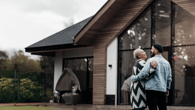 two people laughing and hugging in front of a house