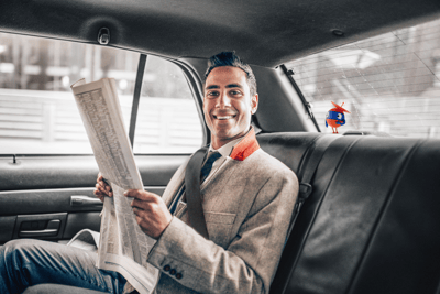 man reading newspaper in back seat of car