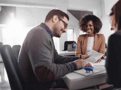 three smiling people sitting around a desk looking at paperwork