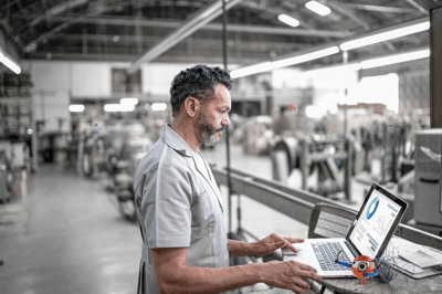 man standing working on a laptop in a manufacturing plant