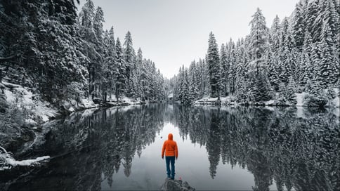 A person in an orange jacket looking at a lake into a valley.