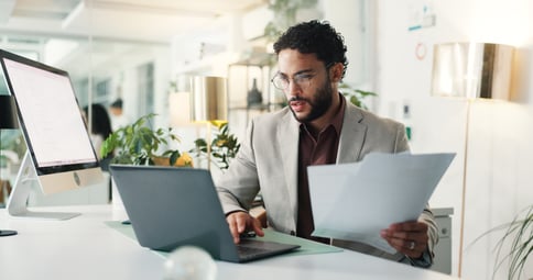 office worker sitting at a desk using a laptop and reviewing documents