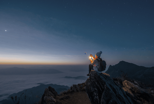 person sitting holding a light outdoors mountaintop starry night 