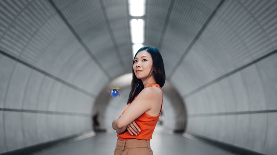 Confident Asian woman standing in a modern tunnel with arms crossed, wearing an orange top—representing women in tech and automation leadership.